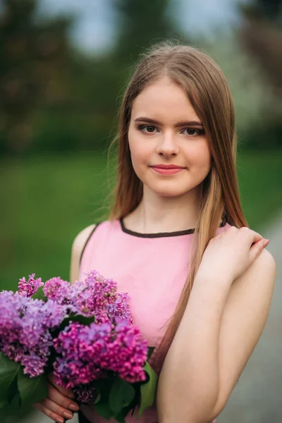 La ragazza di capelli bionda attraente tiene un mazzo di lilla in mani. Affascinante ragazza fuori — Foto Stock