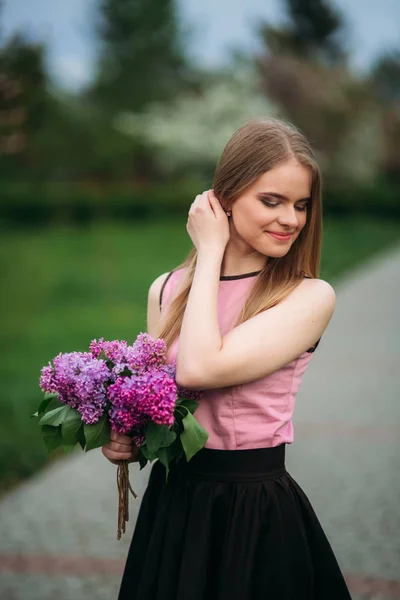 Attractive blond hair girl hold a bouquet of lilac in hands. Charming girl outside — Stock Photo, Image