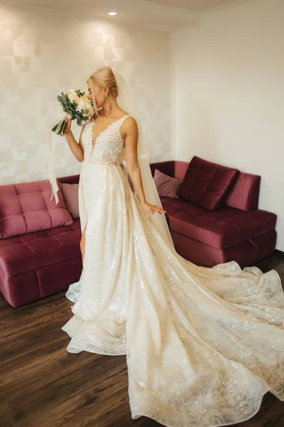 Élégante mariée dans une belle robe de mariée avec bouquet à la maison. Femme aux cheveux blonds avec beau maquillage et coiffure — Photo