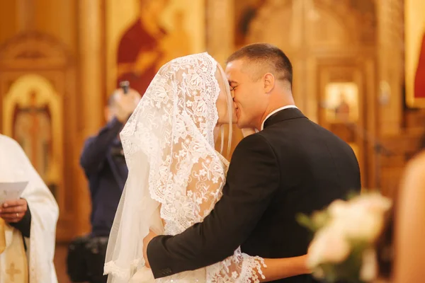 Noivo e noiva beijar uns aos outros na igreja — Fotografia de Stock