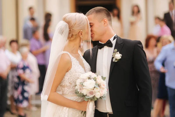 Sposo e sposa si baciano vicino alla chiesa. Sposi novelli in giorno estivo — Foto Stock