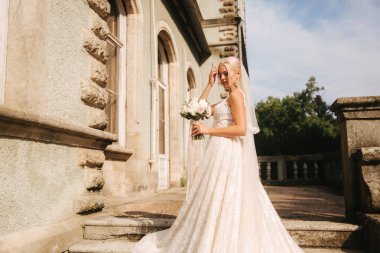 Muhteşem gelin gelinlikle merdivende palace tarafından ayakta. Bir buket çiçek tutun