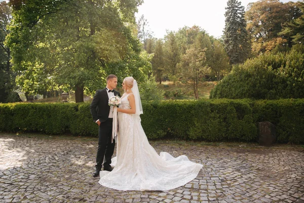 Belo casal de casamentos andando no parque. Noiva com vestido branco longo e noivo elegante — Fotografia de Stock