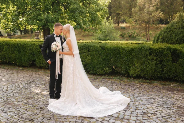 Vackra bröllop par promenader i parken. Brud med lång vit klänning och eleganta brudgummen — Stockfoto
