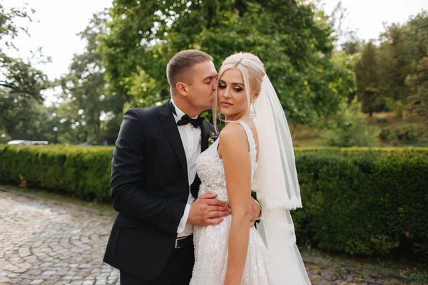 Belo casal de casamentos andando no parque. Noiva com vestido branco longo e noivo elegante — Fotografia de Stock