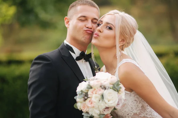 Bonito noivo abraçar sua linda noiva. Recém-casados a passear no parque. Mulher de cabelo loiro em vestido de noiva elegante — Fotografia de Stock