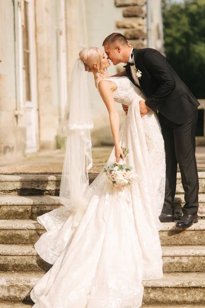 Sposo e sposa in piedi sulle scale. Modella in abiti eleganti. Abito lungo bianco e abito elegante — Foto Stock