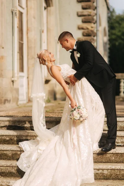 O noivo e a noiva estão nas escadas. Modelo de moda em roupas elegantes. Vestido longo branco e terno elegante — Fotografia de Stock