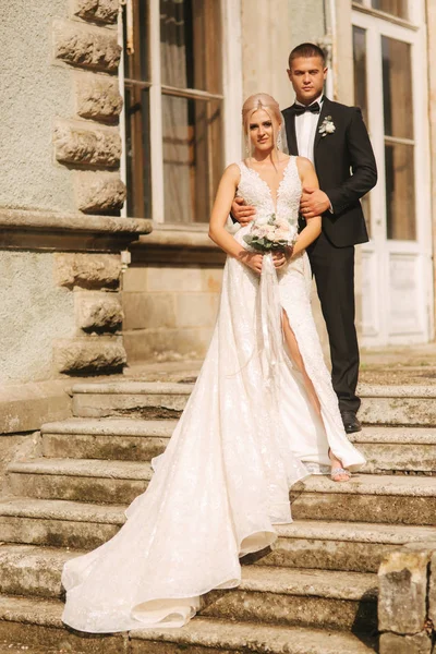 O noivo e a noiva estão nas escadas. Modelo de moda em roupas elegantes. Vestido longo branco e terno elegante — Fotografia de Stock