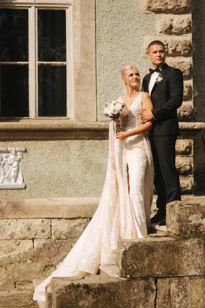 O noivo e a noiva estão nas escadas. Modelo de moda em roupas elegantes. Vestido longo branco e terno elegante — Fotografia de Stock