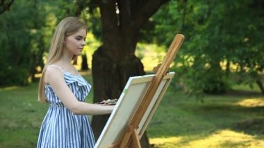 Güzel kız parkta boyalar ve bir spatula ile bir palet kullanarak bir resim çizer. Şövale ve tuval resmi