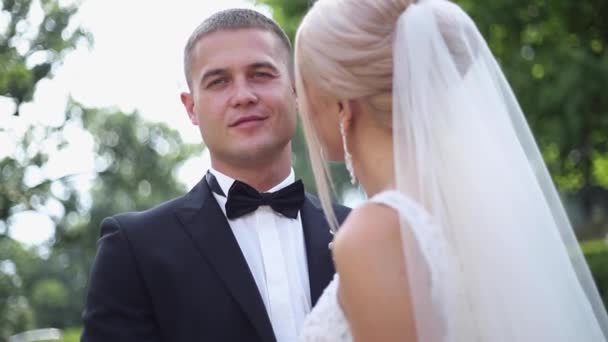 Bonito noivo abraçar sua linda noiva. Recém-casados a passear no parque. Mulher de cabelo loiro em vestido de noiva elegante — Vídeo de Stock