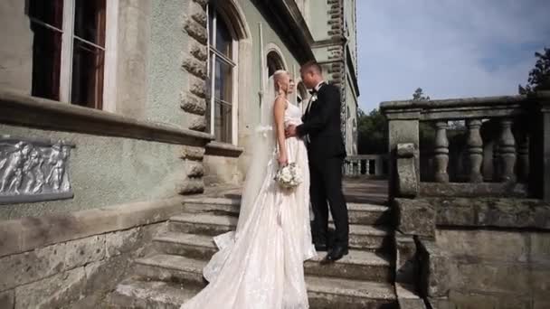 Γαμπρός και νύφη σταθεί σκάλες. Μόδα μοντέλο σε κομψά ρούχα. Λευκό μακρύ φόρεμα και κομψό κοστούμι — Αρχείο Βίντεο