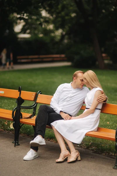 Mooie paar zit op de Bank in het park. Blonde haren man en vrouw besteden tijd togerther. Zij zwarte paraplu. Achtergrond van groen gras — Stockfoto