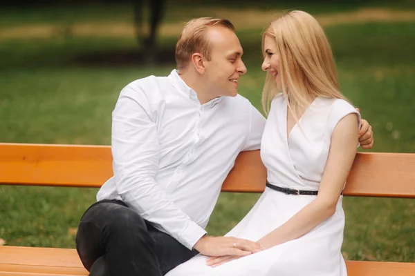 Mooie paar zit op de Bank in het park. Blonde haren man en vrouw besteden tijd togerther. Zij zwarte paraplu. Achtergrond van groen gras — Stockfoto