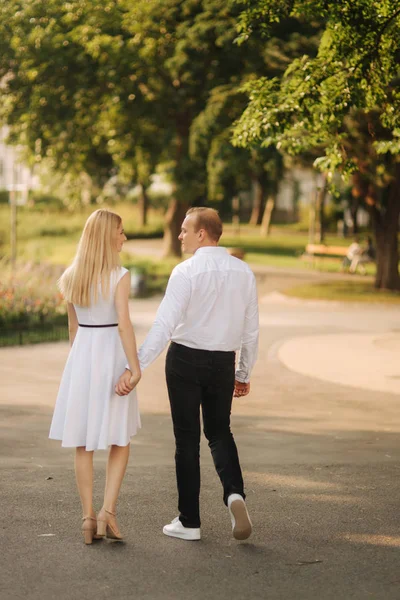 Junges schönes Paar, Mann in weißem Hemd und Frau in Kleid, die im Sommer durch den Park spazieren — Stockfoto