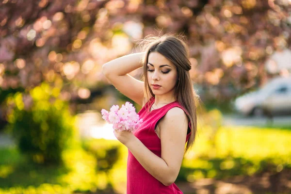 Charmante meisje in mooie roze jurk greep bos van sakura in handen. Mooi Europees meisje in de buurt van de Japanse boom — Stockfoto