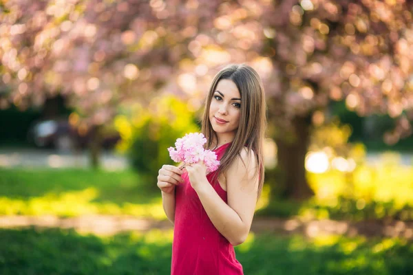 Fuşya bir elbise içinde çekici kız portresi. Onun elinde bir çiçek sakura tutun. Japon ağacının arka plan — Stok fotoğraf