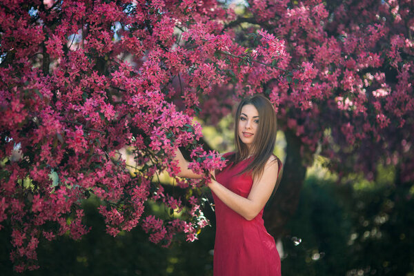 Beautiful lady stand by the big blooming tree voilet color. Happy girl with makeup in spring.