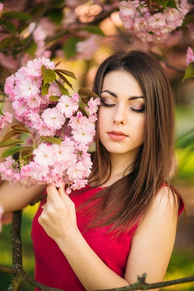 Retrato de una hermosa chica en sakura. Las flores de Sakura rodean a la chica. Una rama de Sakura junto a su cara. Árbol japonés —  Fotos de Stock