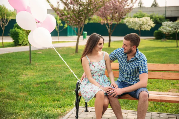 Pár, sedící na lavičce a držet kuličky růžové helia — Stock fotografie