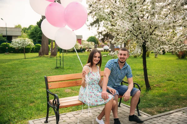 Casal sentado em um banco e segure bolas de hélio rosa — Fotografia de Stock