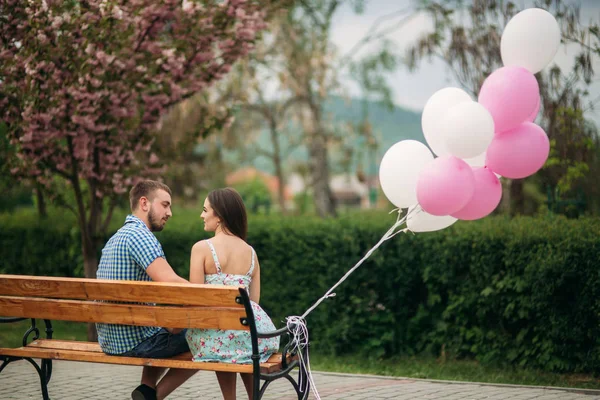 Paar sitzt auf einer Bank und hält rosa Heliumkugeln in der Hand — Stockfoto