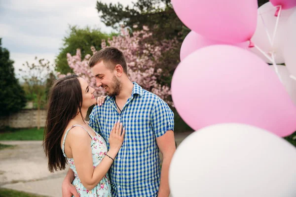 Joven pareja feliz enamorada al aire libre. Hombre guapo y mujer hermosa en un paseo en un parque floreciente primavera. Mantienen bolas de helio. —  Fotos de Stock