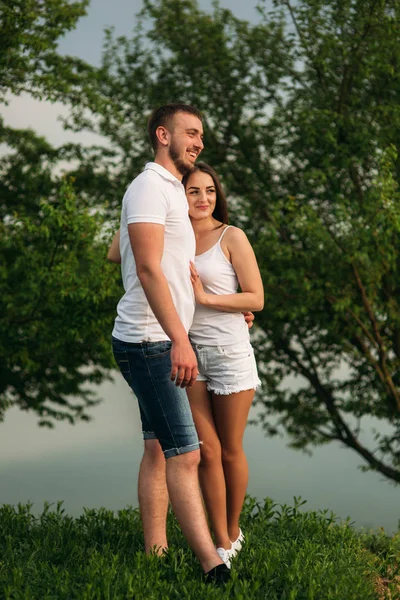 Ein junges Paar in Weiß steht auf dem Hügel. Hintergrund von Bäumen und See — Stockfoto