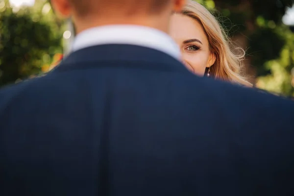 Bruiden is de helft van het gezicht verborgen achter de rug van de bruidegom — Stockfoto