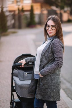 Aile, çocuk ve ebeveyn konsepti-parkta puset ile mutlu anne. Güneş gözlüğü ve şık gri ceket ile anne