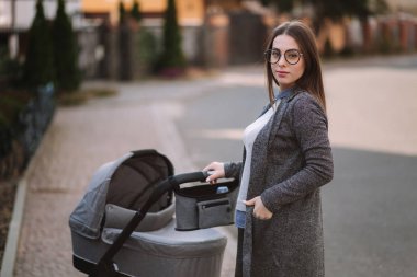 Aile, çocuk ve ebeveyn konsepti-parkta puset ile mutlu anne. Güneş gözlüğü ve şık gri ceket ile anne