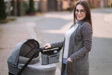 Aile, çocuk ve ebeveyn konsepti-parkta puset ile mutlu anne. Güneş gözlüğü ve şık gri ceket ile anne