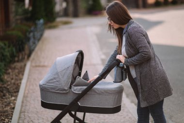 Genç Anne yürümek ile kız içinde Stroller. Annem bebeği önemsiyor. Anne Puset için bakmak ve bebek uyku yardım