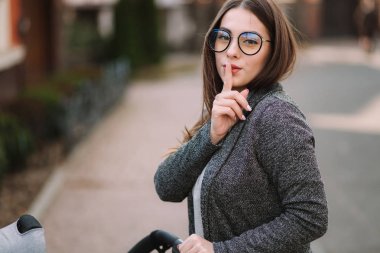 Genç Anne Bebek puset ile yürümek ve dudaklar kadar parmak koyarak ve Shh söylüyor. Anne sessizlik işaret