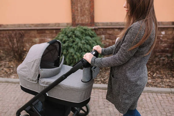 Genç Anne, Bebek arabası içinde yenidoğan bebeği ile yürüyor. Gri bir Pram. Güzel anne içinde Sunglasses