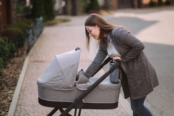 Young mom walking with daughter in stroller. Mother cares for the baby. Mom look in to the stroller and help baby to sleep