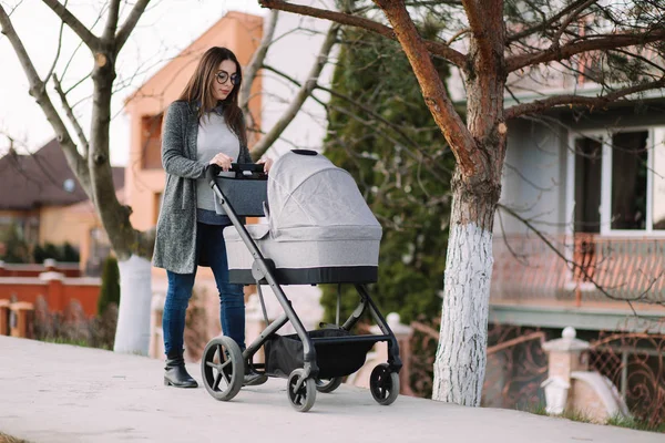 Mamá joven caminando con cochecito en el parque. Elegante madre con bebé — Foto de Stock