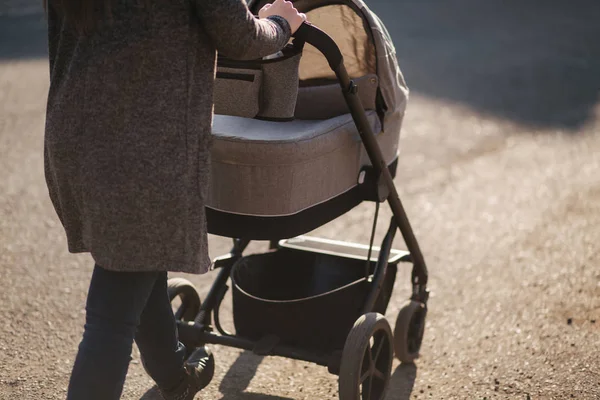 Vista trasera de la madre caminando con su bebé en cochecito. Cochecito gris afuera, puesta de sol — Foto de Stock