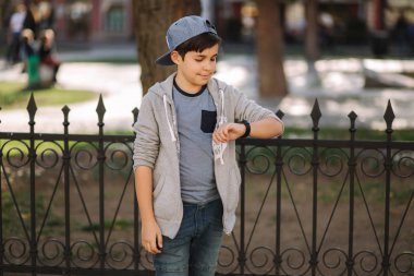 Çocuk saatle bakıyor. Şehirde yürüyen genç çocuk