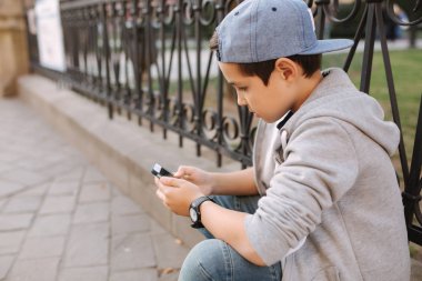 Genç çocuk oyun online oyun dışında smartphone. Şehir merkezinde oturan çocuk. Oğlan oyun oyun süre onun anne gidiş için The dükkan
