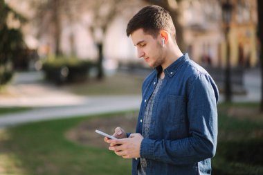 Genç adam sosyal ağda telefon ve kablosuz kulaklıklar ve yazdırma mesajı kullanın
