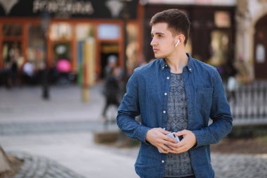 Kablosuz kulaklıklar ile mavi kot gömlek genç şık adam. Adam müzik dinliyor