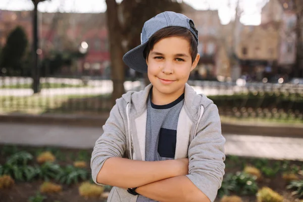 Κομψό μικρό σχολείο αγόρι με μπλε καπάκι που ποζάρει έξω για φωτογραφία. Αγόρι με τα πόδια στην πόλη στον καλοκαιρινό καιρό — Φωτογραφία Αρχείου