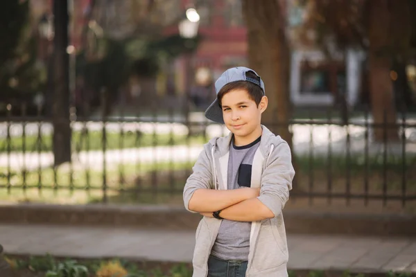 写真のために外でポーズをブルーキャップでスタイリッシュな小さな学校の男の子。スパン夏の天気の街を歩いている少年 — ストック写真
