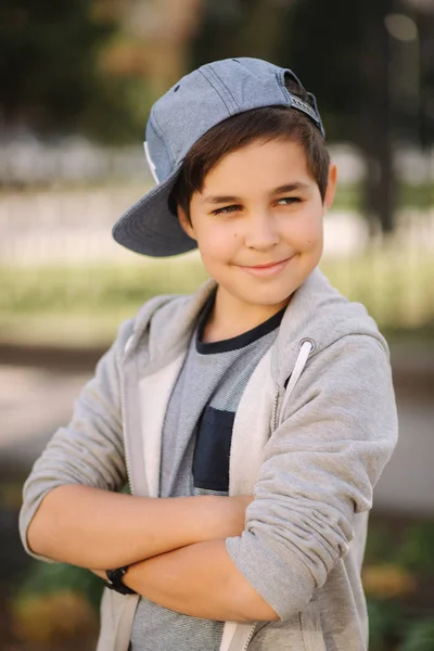 Elegante niño de escuela en gorra azul posando afuera para la foto. Niño caminando en la ciudad en el tiempo sping verano —  Fotos de Stock