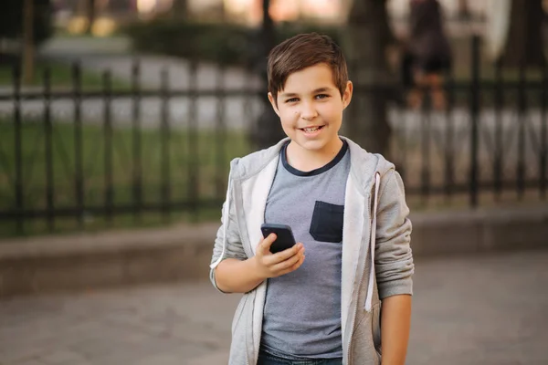 Vooraanzicht van lachen tiener jongen staan in de stad met smartphone — Stockfoto