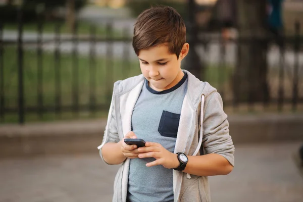 Ung pojke som leker med smaptphone. Schoolboy använder mobil telefon på gatan — Stockfoto