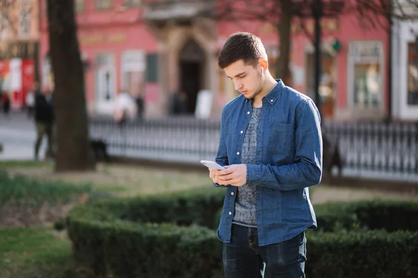 Les jeunes hommes utilisent le téléphone et les écouteurs sans fil et impriment des messages sur les réseaux sociaux — Photo