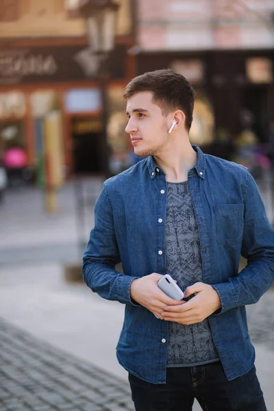 Joven hombre con estilo en camisa vaqueros azules con auriculares inalámbricos. Hombre escuchando una música — Foto de Stock